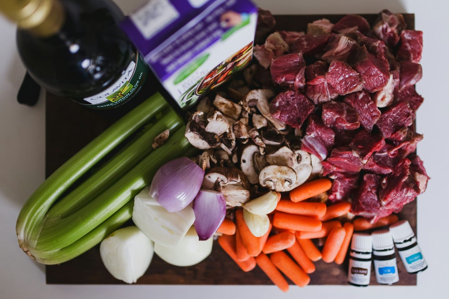Carne de res cruda, verduras e ingredientes sobre una tabla de cortar de madera.